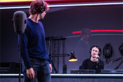 Lucas Iverson in the studio, with Owen Campbell in the booth behind, in A Ghost in Your Ear. Photo by Matthew Murphy