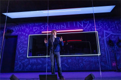 Lucas Iverson at the microphone before a chalk-scrawled wall in A Ghost in Your Ear. Photo by Matthew Murphy