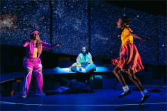 A performer in a pink tracksuit and a girl leap beneath a starfield as a woman sits between them in creation stories and all the important importants. Photo by Valerie Terranova