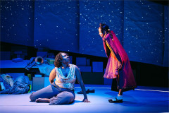 A woman seated on the floor looks up at a girl in a red cape under a starry sky in creation stories and all the important importants. Photo by Valerie Terranova
