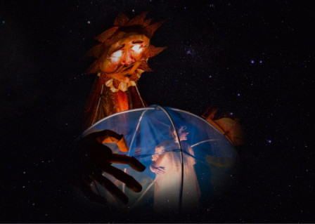 A sun puppet looks down on a lit globe in Starcadia