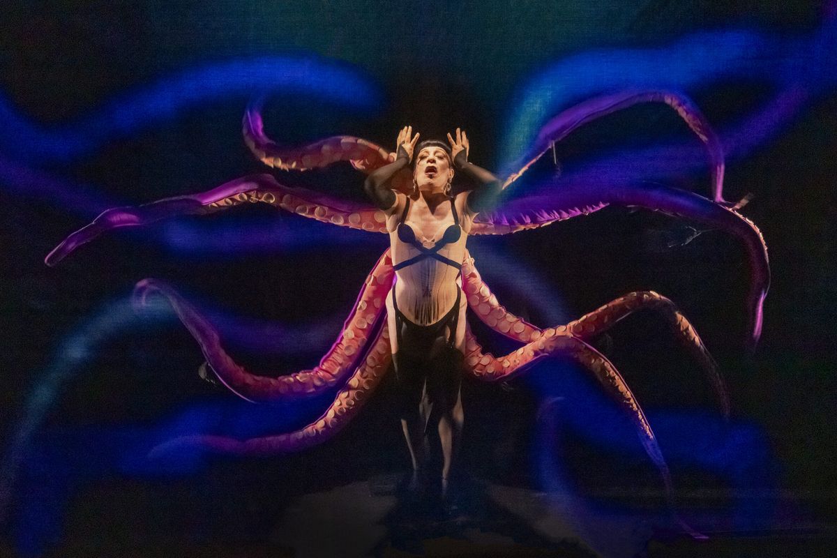 Joey Arias in a corset at the centre of a dark stage, flanked by huge writhing octopus arms