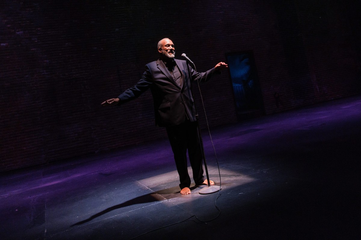 Smith stands barefoot in a pool of purple light beside the microphone stand, one arm flung out behind him