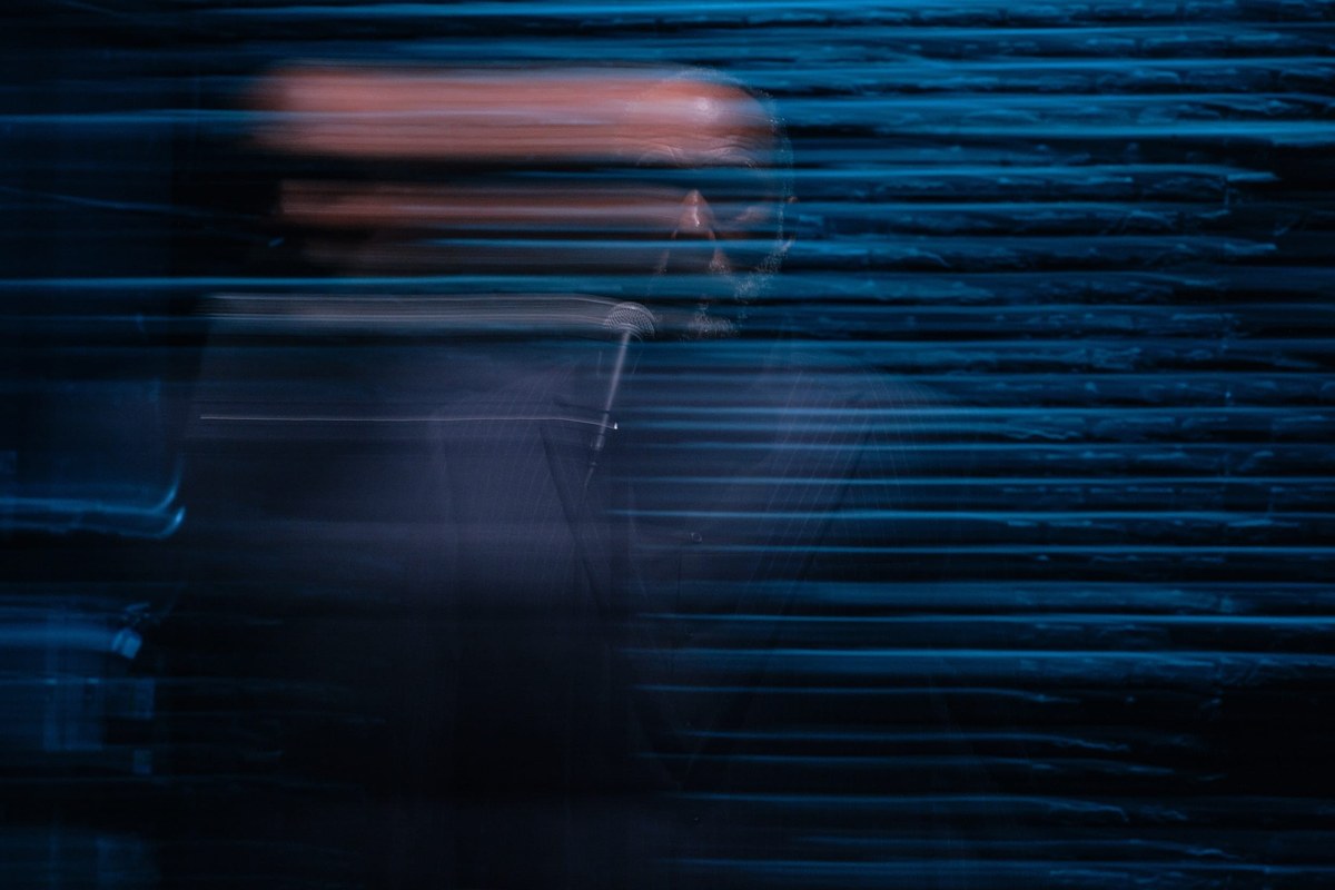 A long-exposure blur of Smith at the microphone under blue light, his figure smeared into streaks