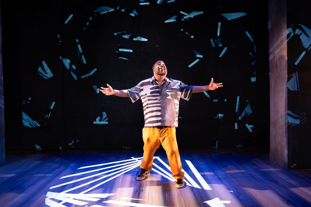 Jacob Ming-Trent, arms flung wide in a pool of light, as sheets of paper fall around him