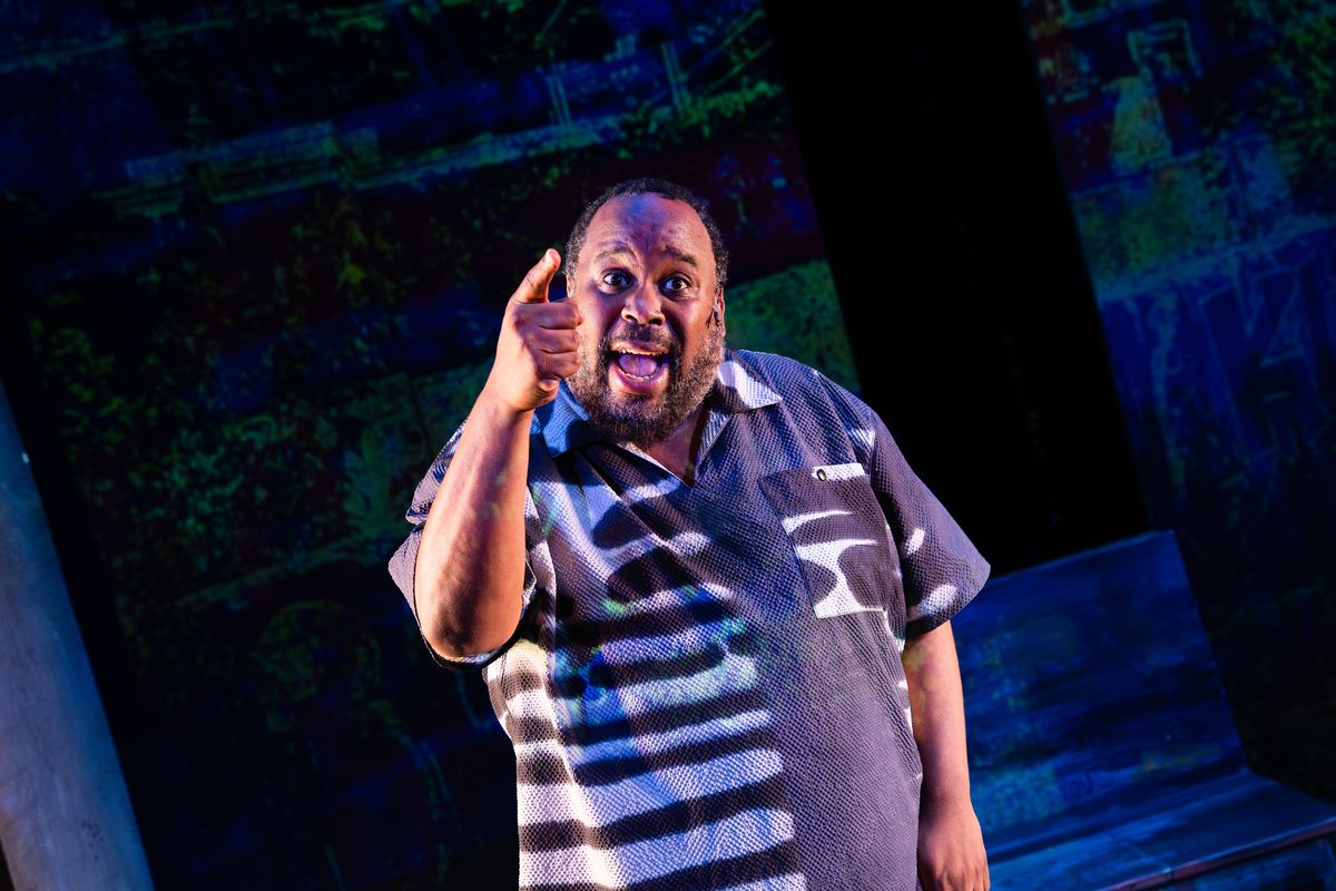Jacob Ming-Trent in close-up, one finger raised, mid-speech against a blue projection
