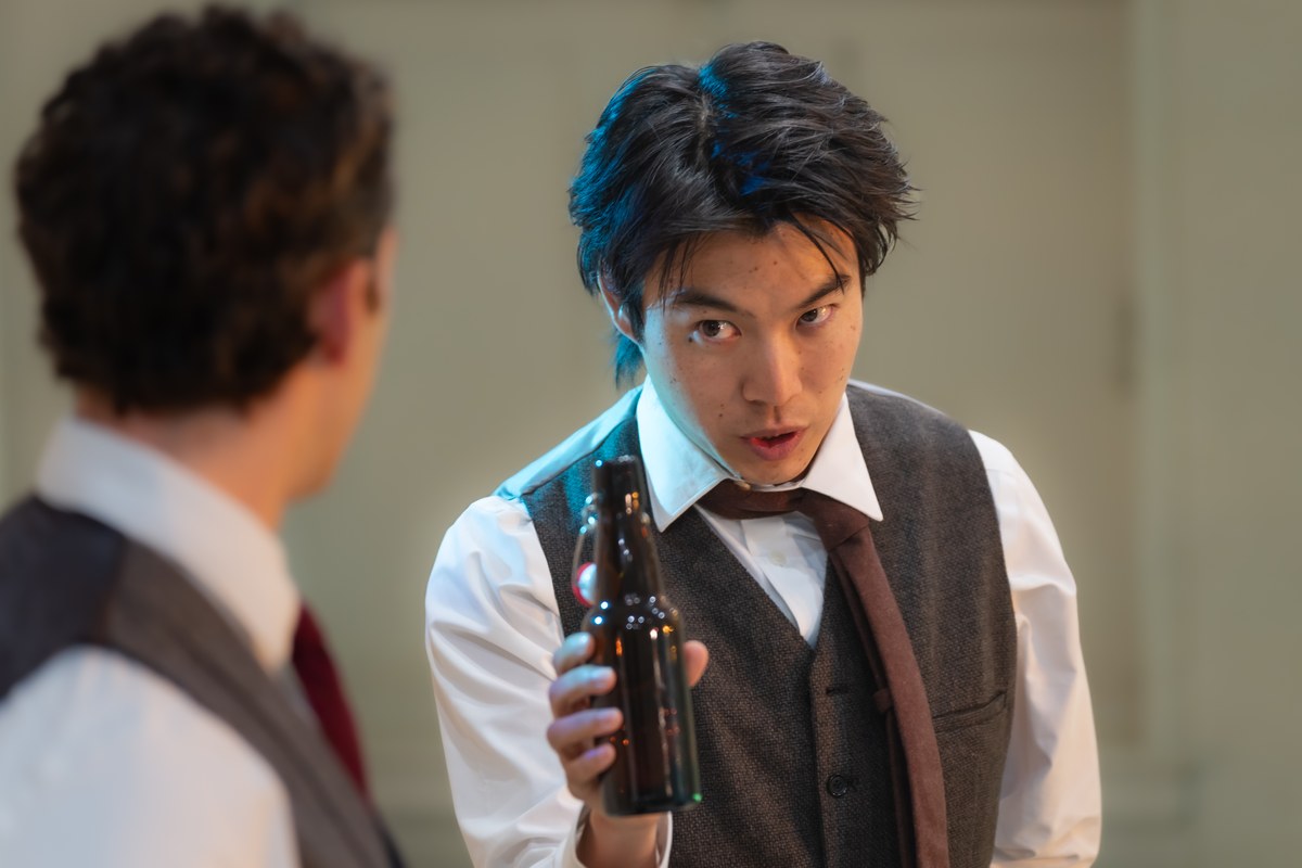 Yaron Lotan as the young Housman, holding a bottle mid-conversation with a fellow Oxford student