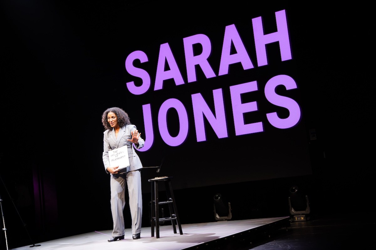 Sarah Jones on stage beneath her name in giant letters in America, Who Hurt You? at the Polonsky Shakespeare Center. Photo by HanJie Chow Sarah Jones on stage beneath her name in giant letters in America, Who Hurt You? at the Polonsky Shakespeare Center. Photo by HanJie Chow