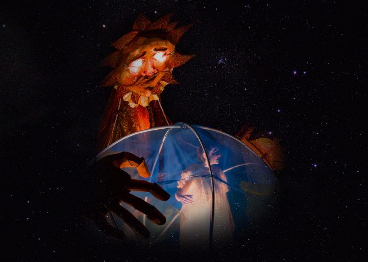 A sun puppet looks down on a lit globe in Starcadia